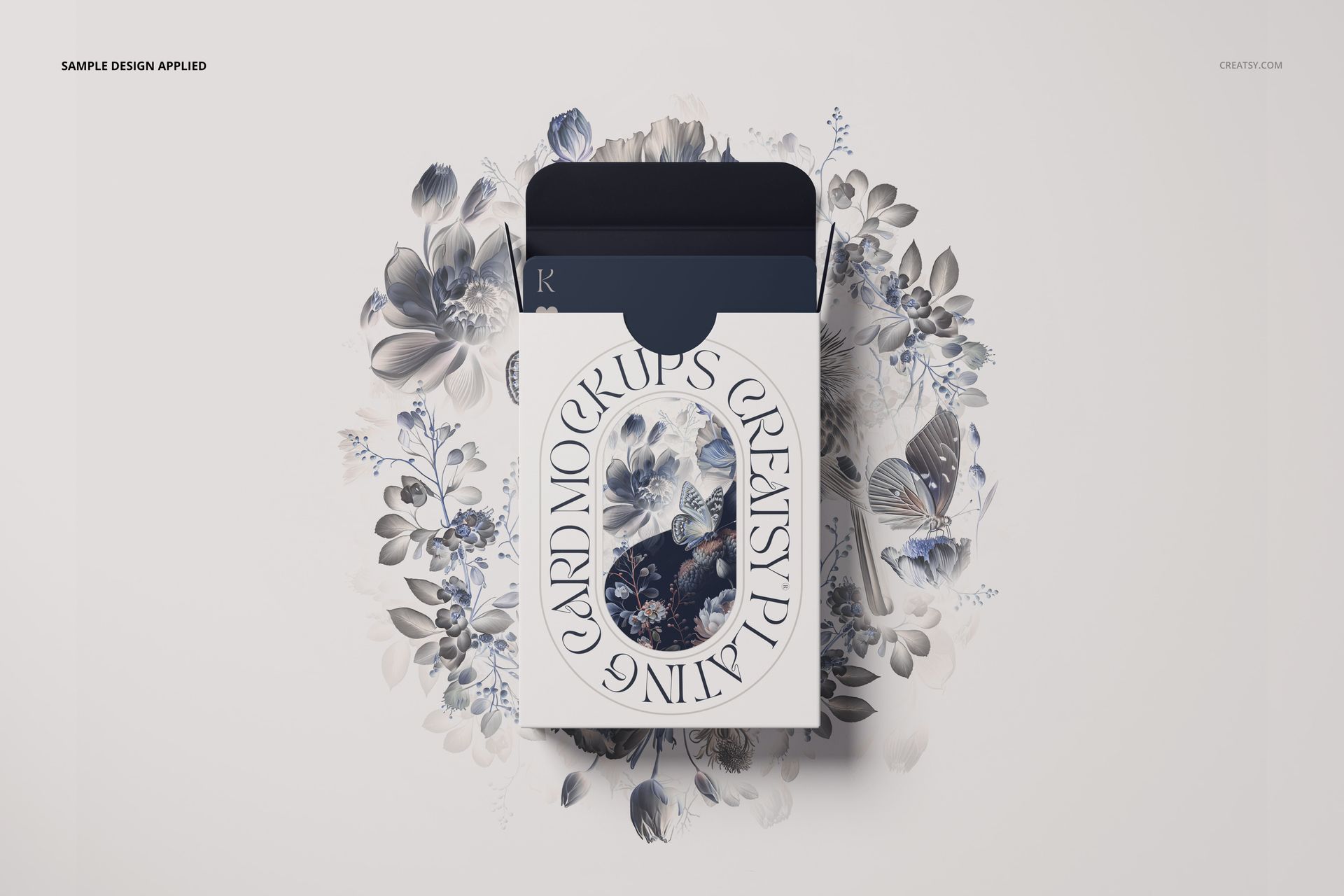 Front view of a playing cards box mockup with floral artwork in blue and gray tones, surrounded by matching flowers.