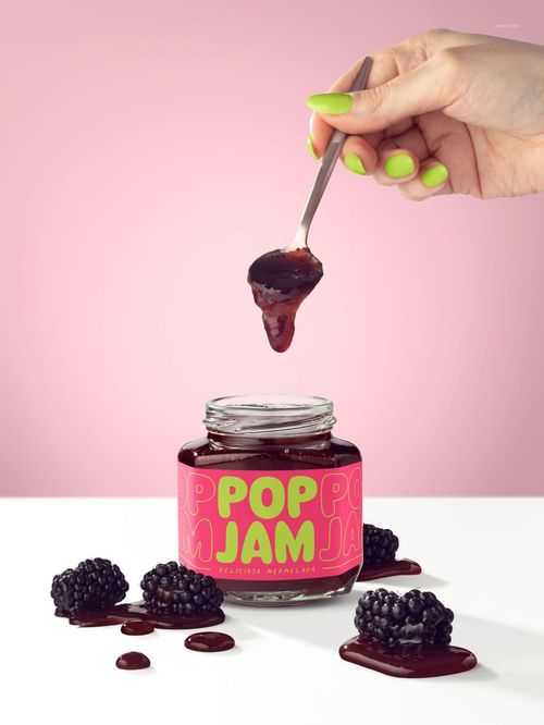 Close-up of a blackberry jam jar mockup with vibrant label, jam on a spoon, and fresh blackberries on a white surface.