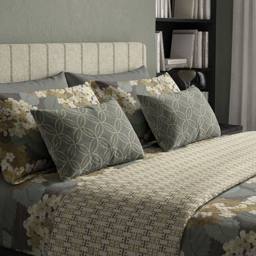Bedding mockup featuring a neatly made bed with patterned pillows and duvet in earthy tones, set against a textured headboard and bookshelf background.
