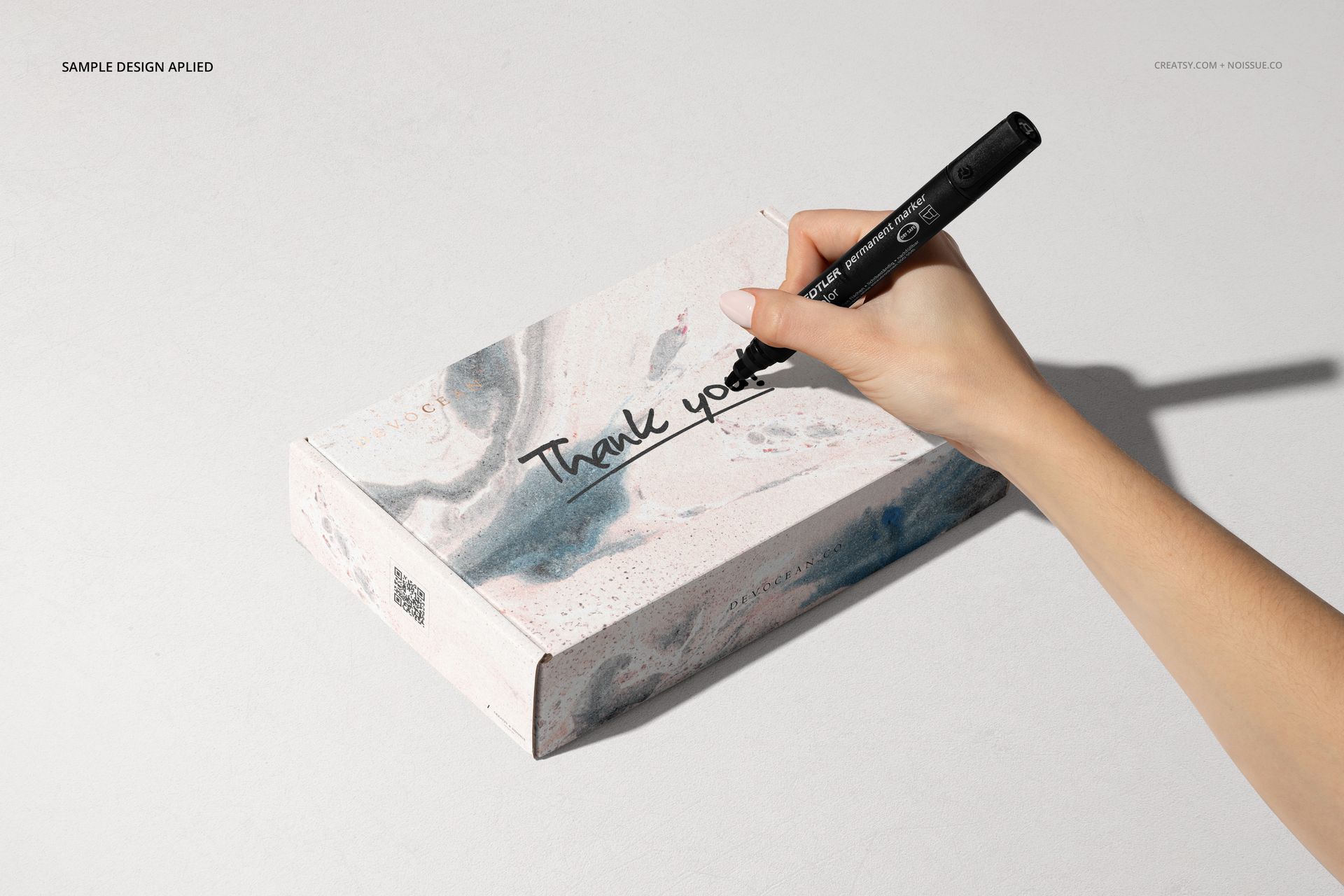 Noissue mailing box PSD mockup with abstract marble design, viewed from above with a hand holding a black marker.