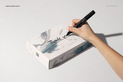 Noissue mailing box PSD mockup with abstract marble design, viewed from above with a hand holding a black marker.