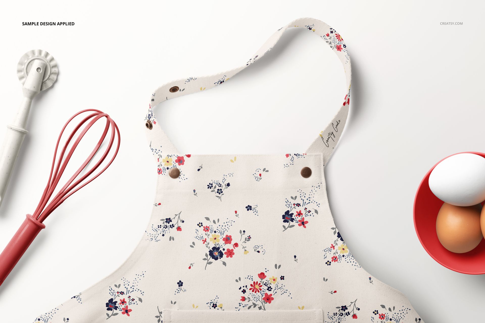 Kids apron with a floral pattern displayed in a top view mockup, surrounded by baking tools and a bowl of eggs.