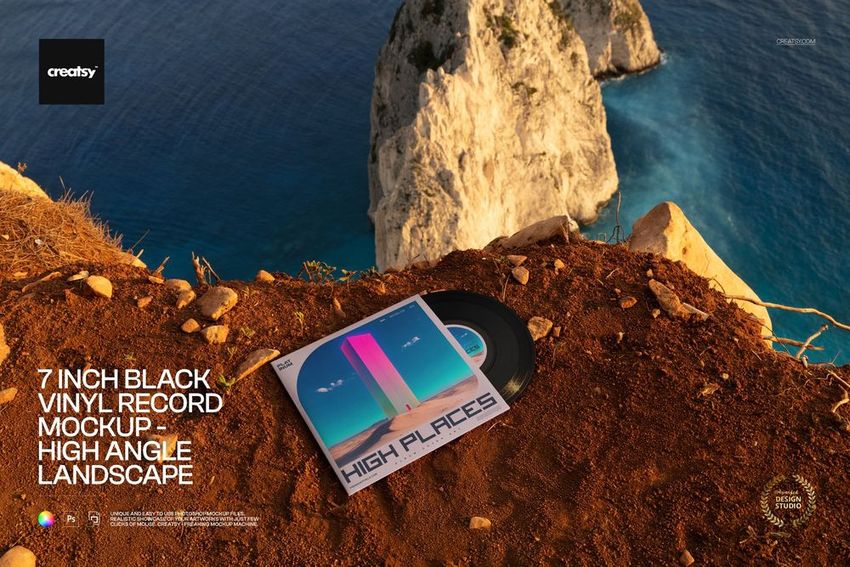 PSD mockup showing a 7 inch black vinyl record and illustrated sleeve resting on rugged ground overlooking blue water.