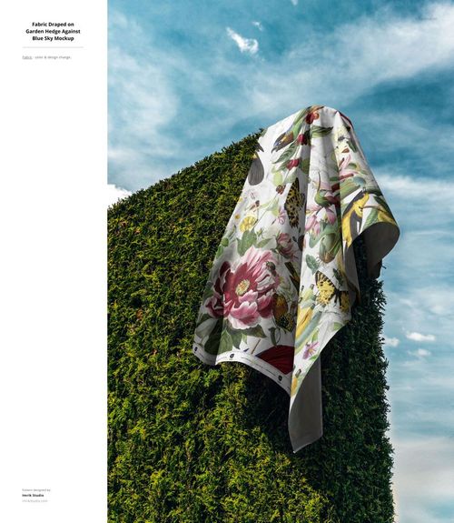 PSD mockup showing a large piece of fabric with botanical design hanging on a garden hedge, outdoor setting with sky view.