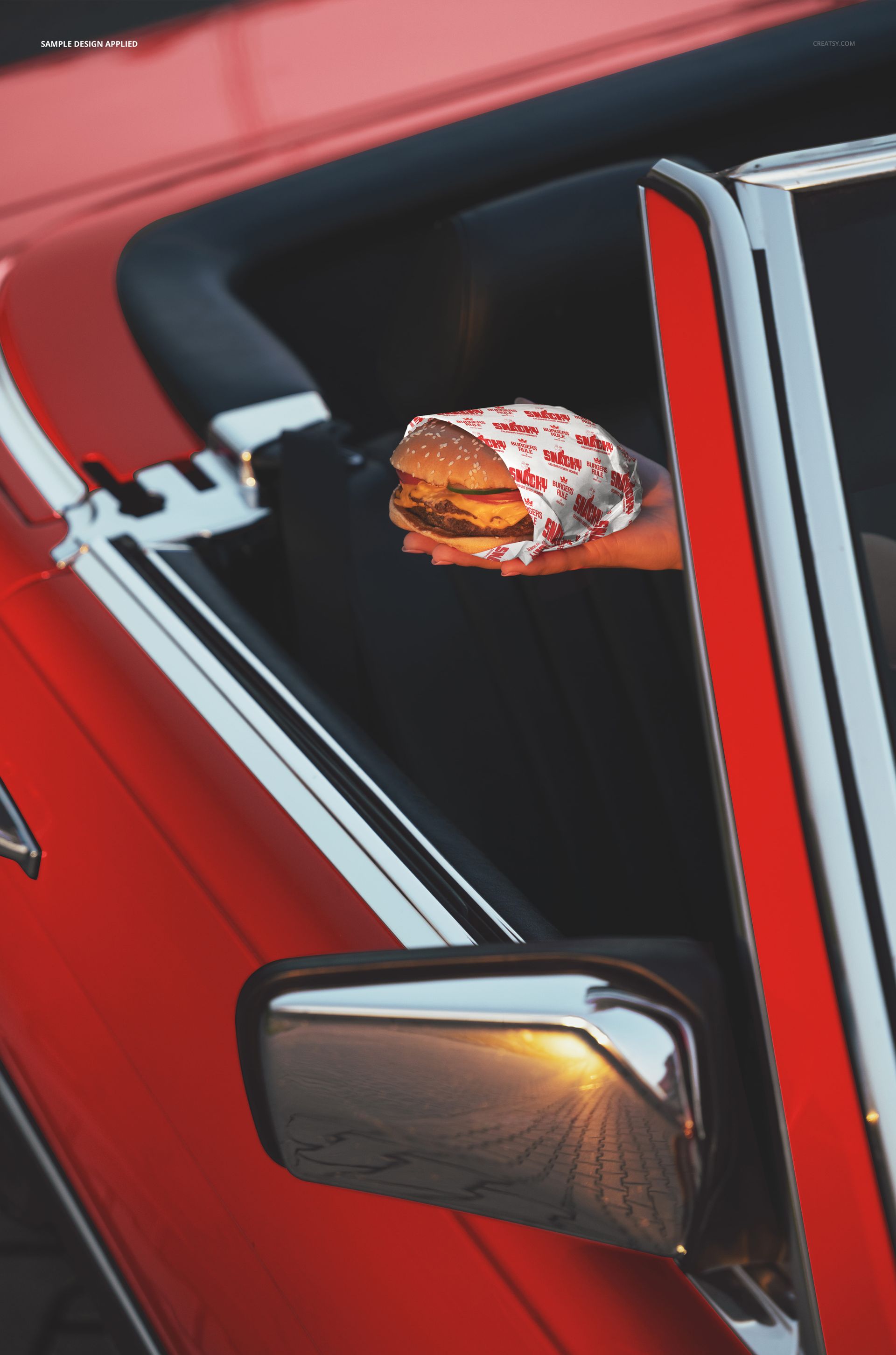 PSD mockup showing a burger in branded paper held from inside a red convertible car, with chrome details visible.