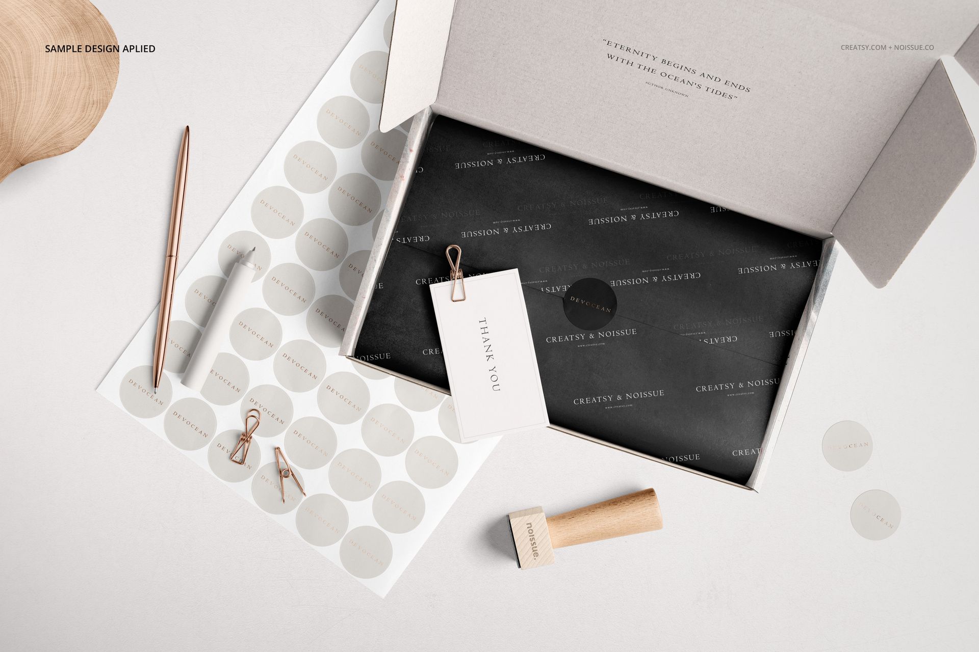 Open mailing box mockup with black tissue paper, thank you card, pen, stamp, and round sticker sheets on a light surface.