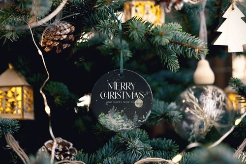 Round ceramic Christmas ornament mockup hanging on a decorated tree, featuring a dark festive design and pine branches.