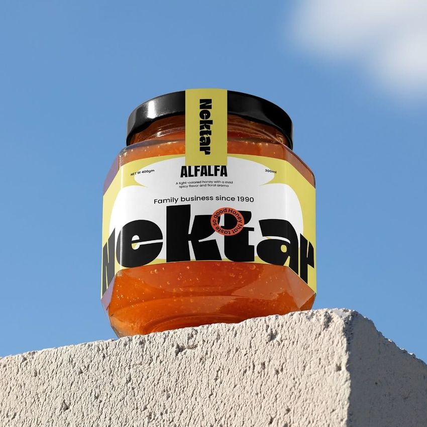 Apricot jam jar mockup with a bold yellow and black label, placed on a textured concrete block against a clear blue sky.