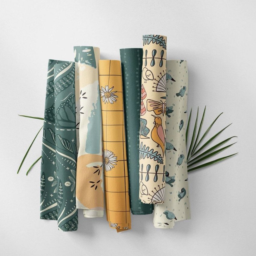 Fabric rolls mockup featuring six patterned fabric rolls arranged side by side on a light surface with green leaves underneath.