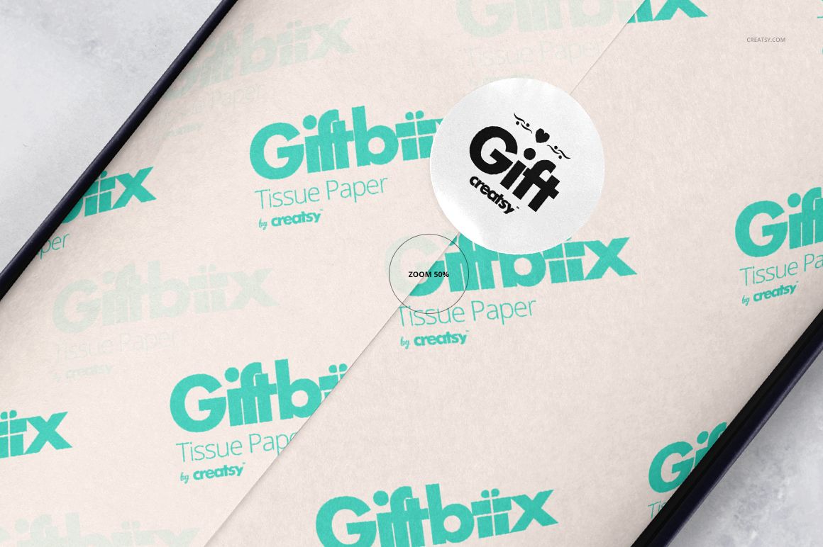 Gift box mockup showing white wrapping tissue paper with teal graphics and a round sticker, seen from a top angle.