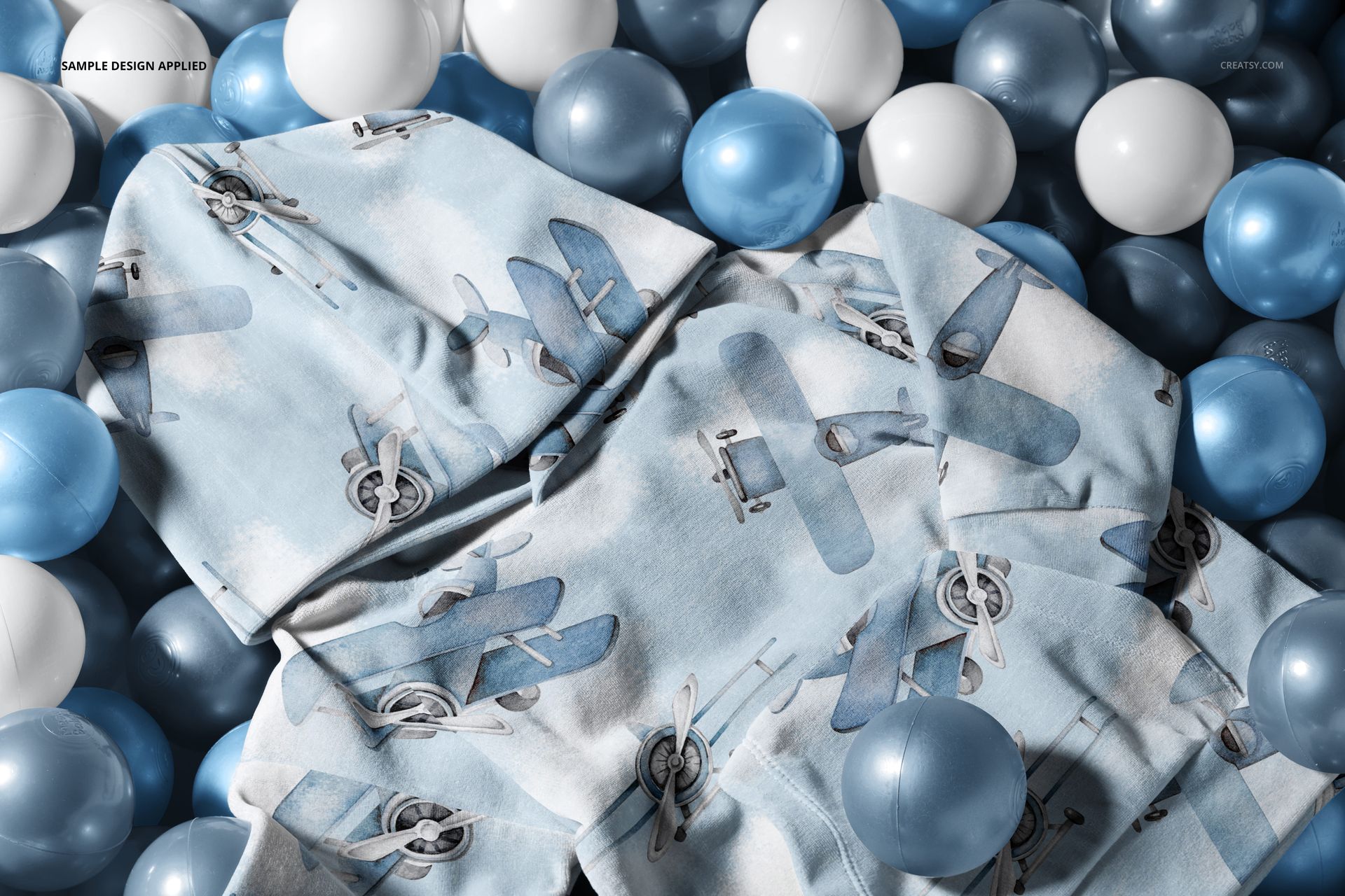 Mockup of a baby velvet velour tracksuit featuring airplane graphics, surrounded by blue and white balls, overhead angle.