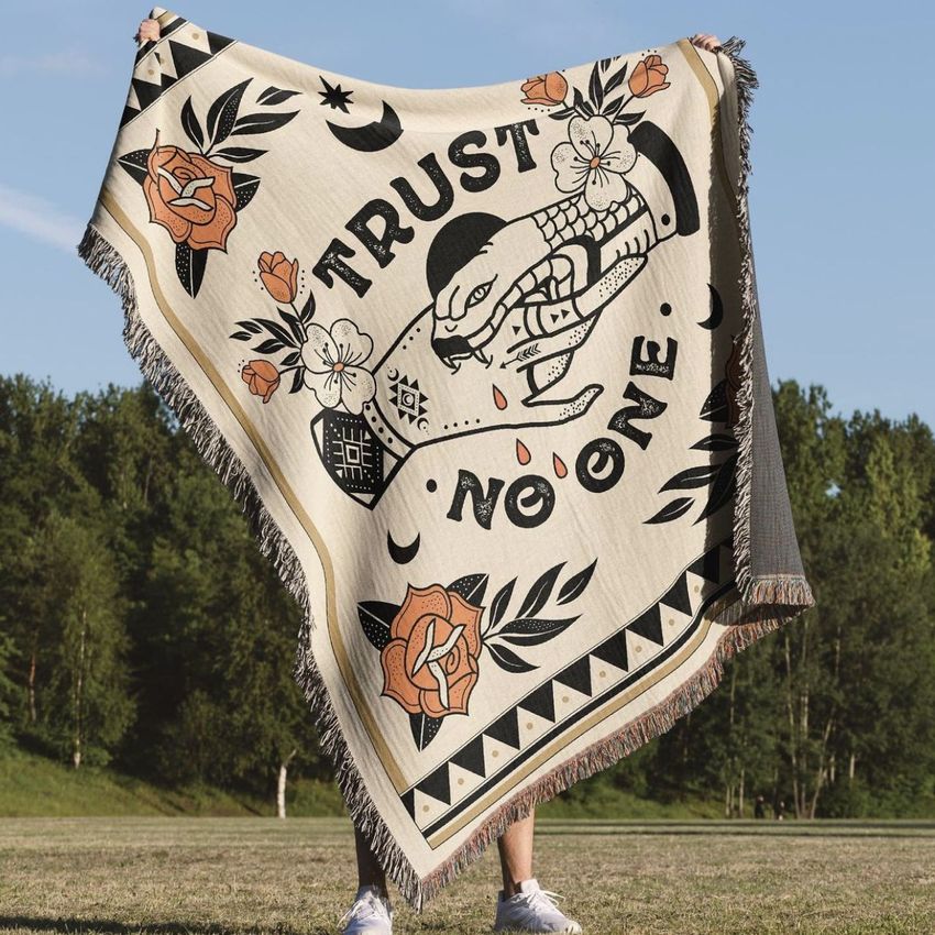 Person outdoors holding a jacquard fringed woven throw blanket mockup with a bold snake and flower design and large text.