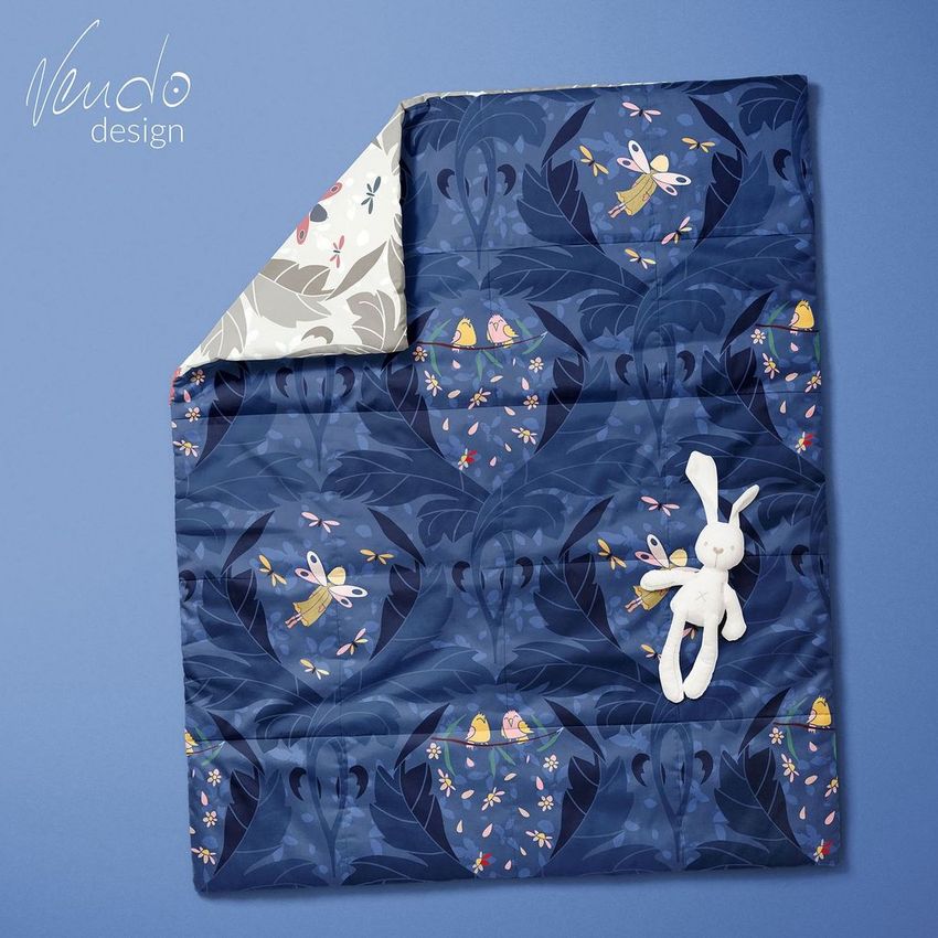 Baby patchwork quilt mockup featuring a blue quilt with whimsical fairy and floral patterns, shown on a blue background with a plush bunny toy.