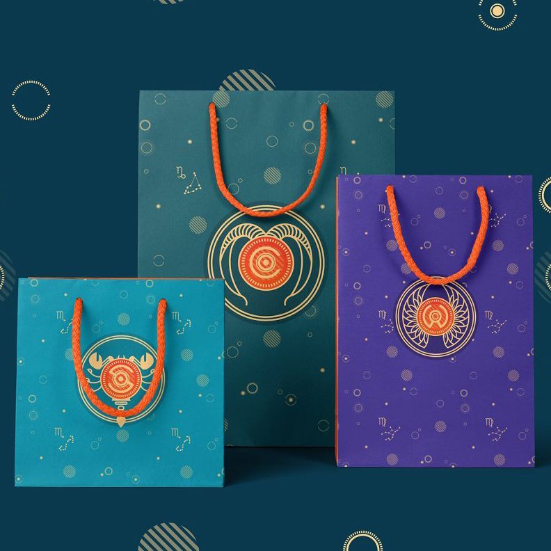 Paper bags mockup featuring three bags with zodiac-inspired designs, arranged upright on a dark blue background with orange handles.