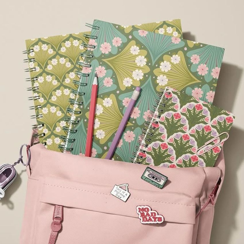 School backpack mockup in light pink with spiral notebooks featuring green and pink scallop patterns, plus two pencils inside.