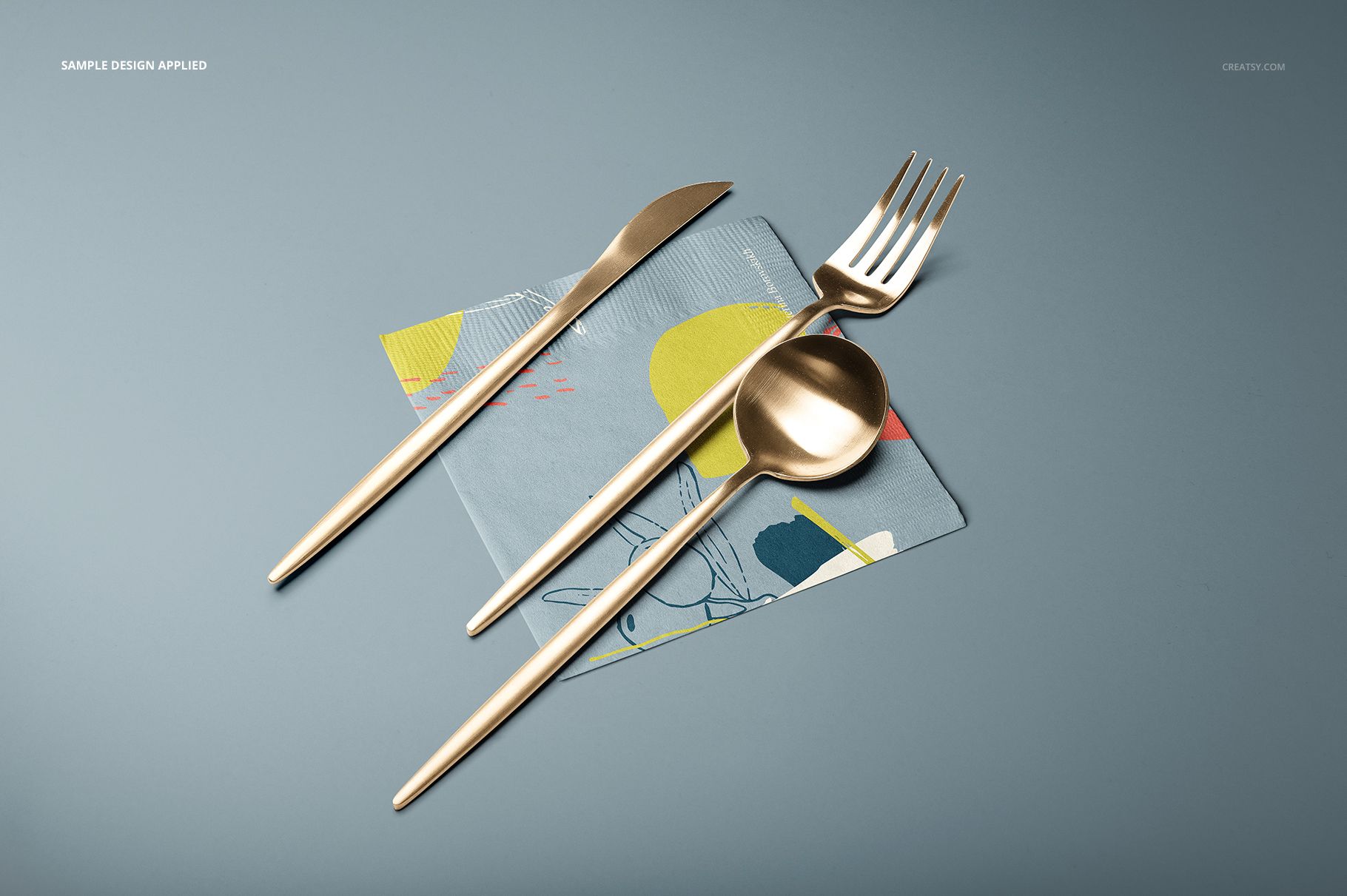 Top view of a paper napkin mockup featuring a modern design, with gold fork, knife, and spoon on a blue background.