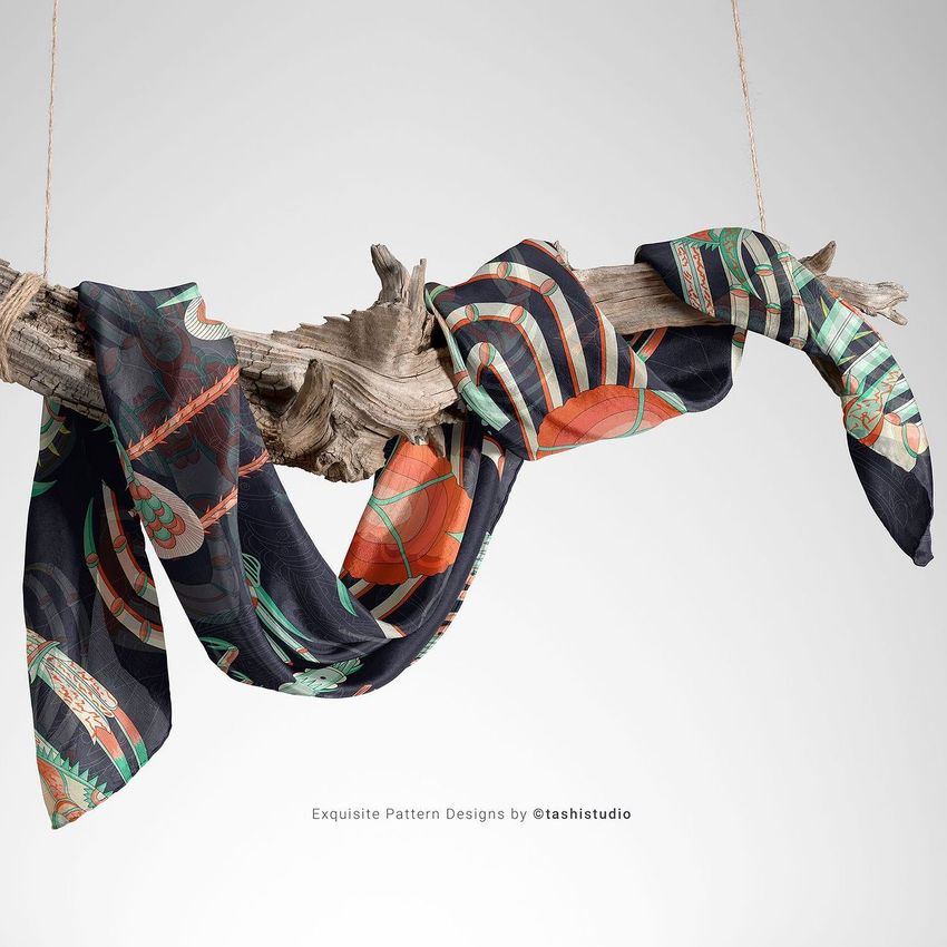 Silk scarf mockup draped over a piece of driftwood, featuring bold geometric and organic patterns in orange, green, and black.