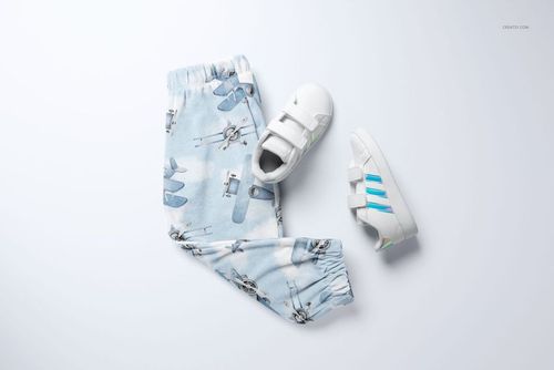 PSD mockup of baby velour tracksuit pants with aviation-themed print, paired with white sneakers on a white backdrop.