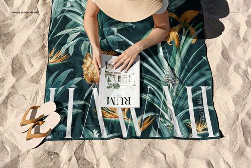 Beach towel mockup featuring green foliage and pineapple design, person in sun hat reading on sandy beach.