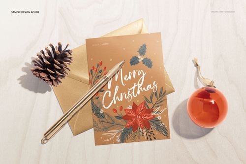 Stationery mockup featuring a gold envelope, holiday card with floral and berry design, pen, pinecone, and ornament on a light wood surface.