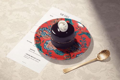 Round ceramic plate with vibrant red floral pattern, holding a glossy chocolate dessert, viewed from above.