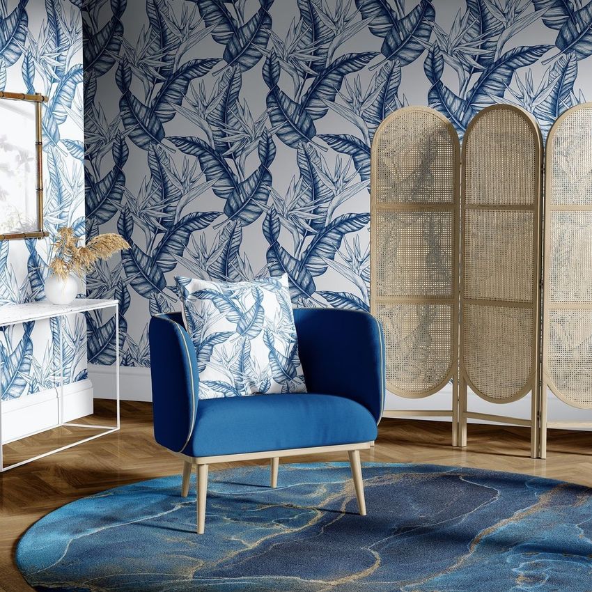 Armchair mockup in a sitting corner with blue upholstery, patterned cushion, and blue botanical wallpaper, next to a woven room divider.