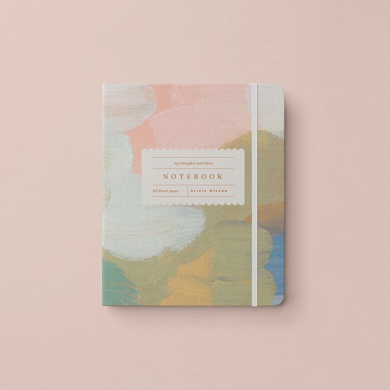 Stationery mockup showing a notebook with an abstract painted cover in pastel colors on a light pink background.