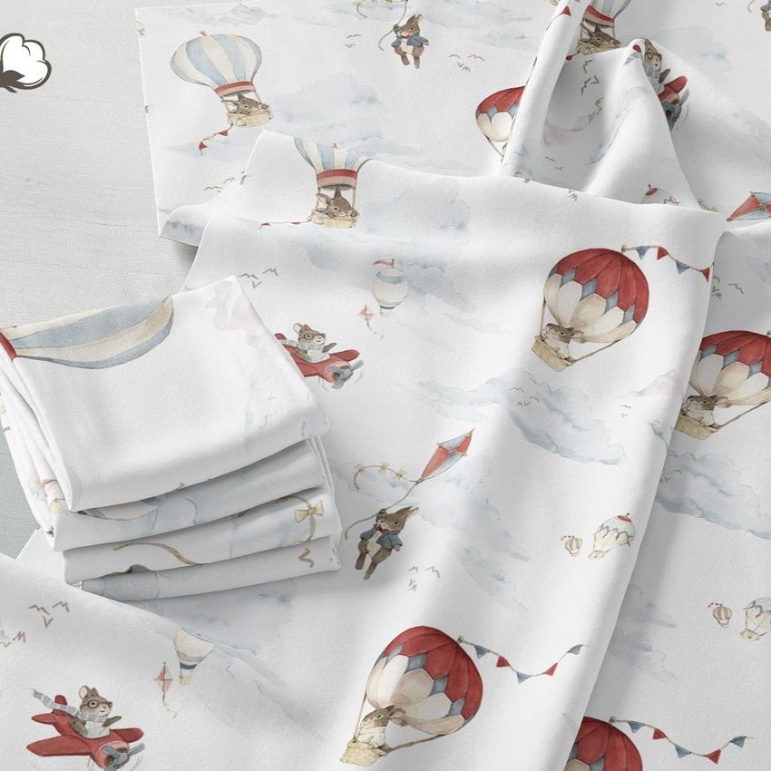 Folded fabrics mockup showing white cloth with whimsical hot air balloon and animal illustrations in red, blue, and gray tones.
