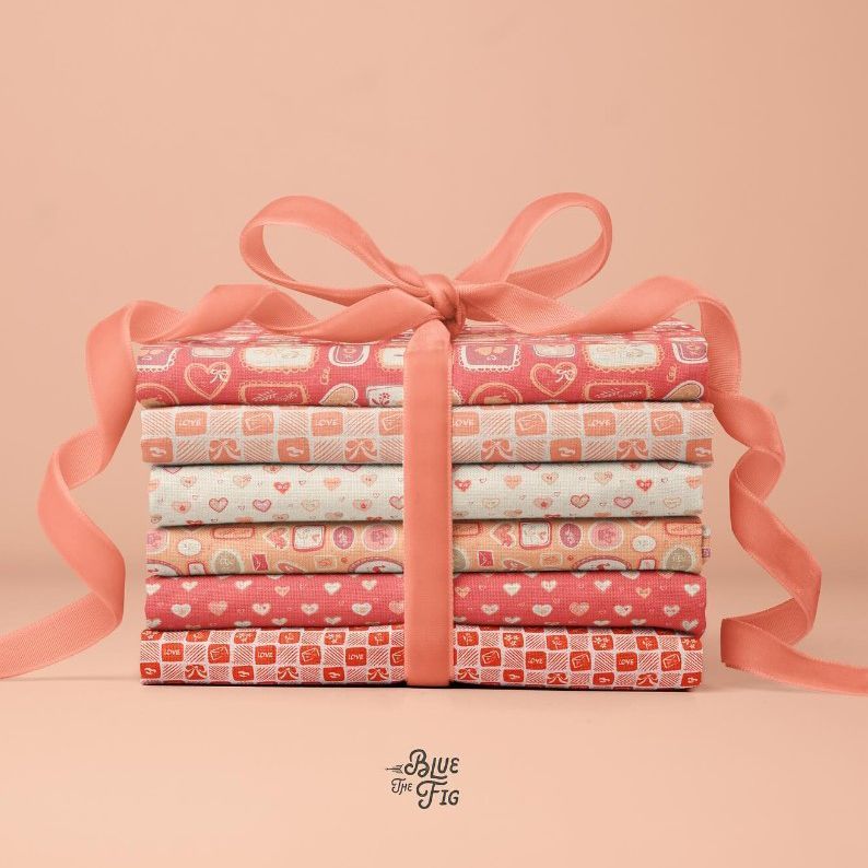 Fabric stack mockup featuring neatly folded patterned fabrics in red and cream tones, tied with a wide pink ribbon bow.