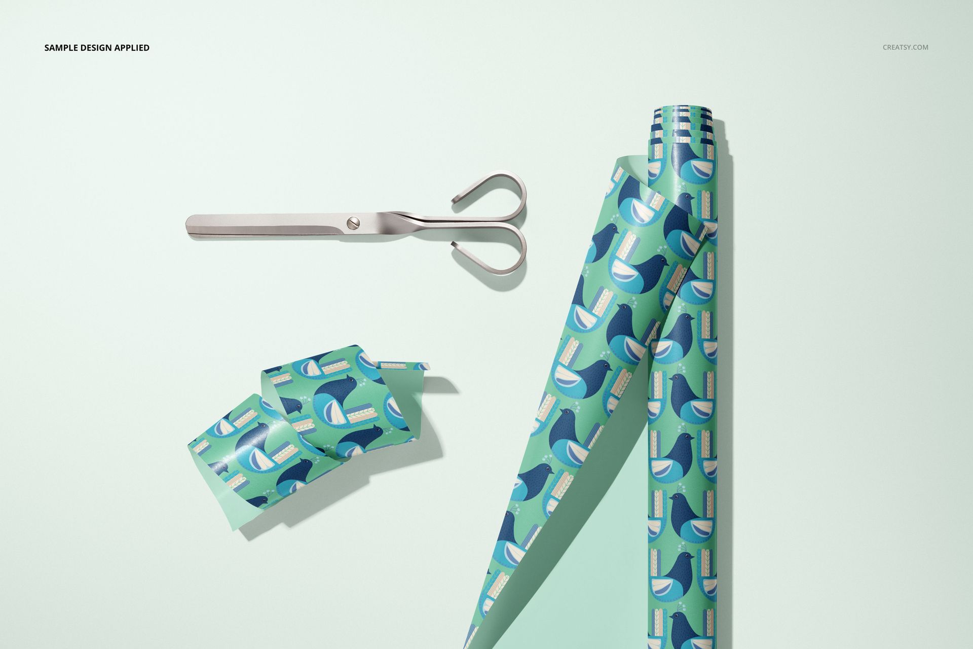 Gift wrapping paper mockup featuring rolls and cut pieces with a blue geometric design, displayed with metal scissors.