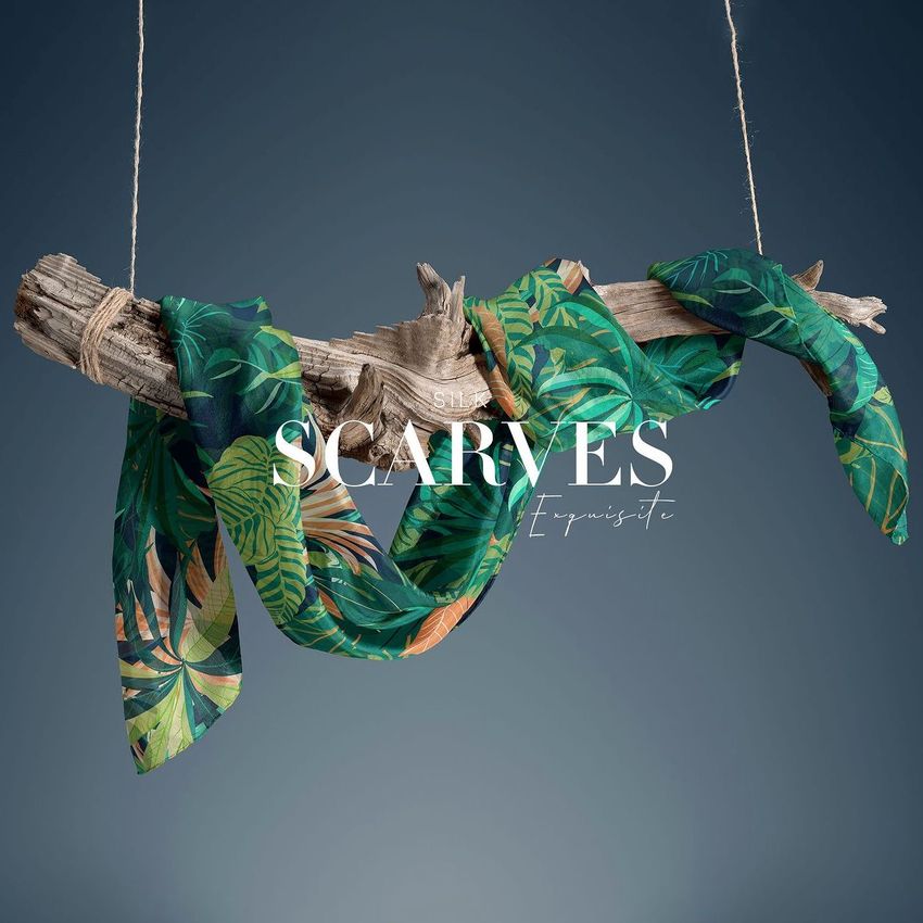 Silk scarf mockup draped over a piece of driftwood, featuring a lush green tropical leaf pattern on a blue background.