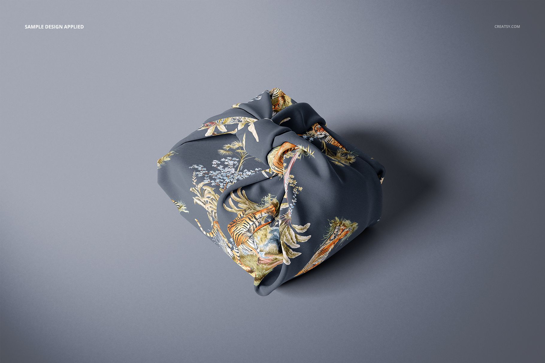 Fabric gift wrap mockup featuring a neatly wrapped square package with a dark floral pattern, viewed from above on a gray surface.