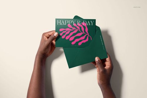 Close-up of hands displaying a 5x7 greeting card mockup set featuring a green card with pink pattern and envelope.