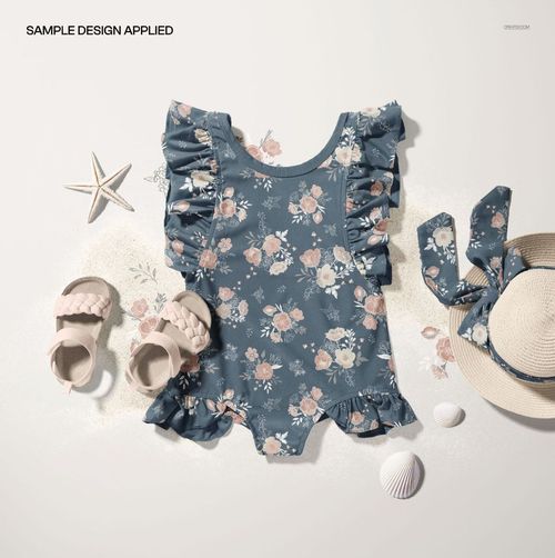 Flat-lay of a floral baby swimsuit and bow hat mockup, styled with sandals, starfish, and scattered seashells.