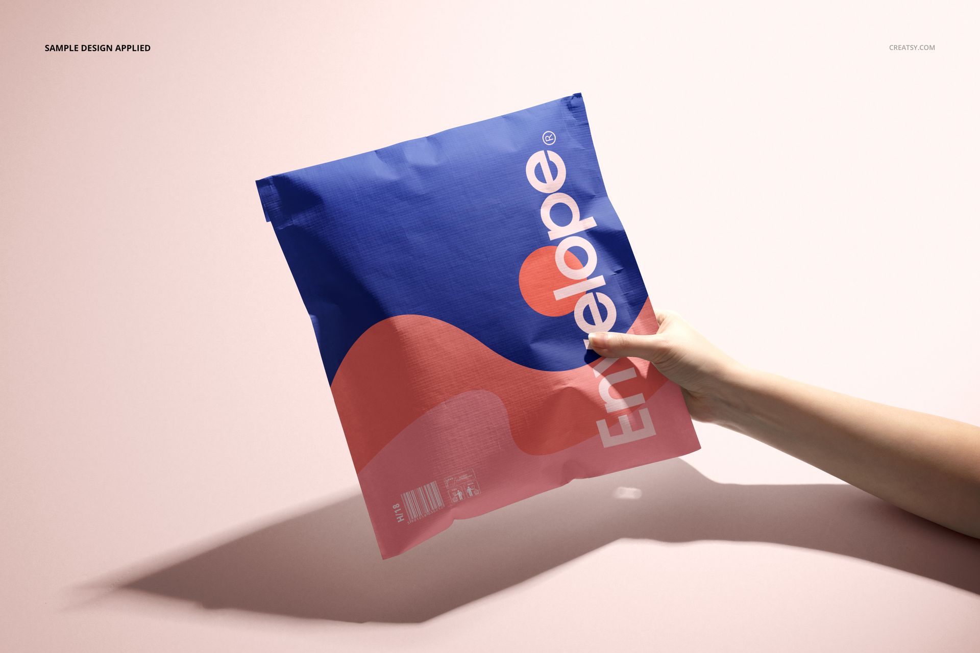 Front view of a cloth lined envelope mockup with bold blue and pink design, held by a hand on a pale backdrop.