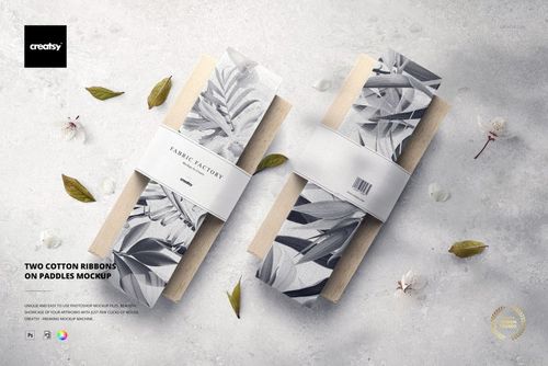 Mockup of two fabric ribbons featuring monochrome botanical designs, each secured to wooden paddles in a front view.