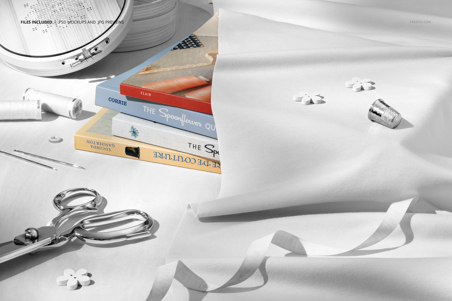 Flat lay of a sewing area featuring white jersey fabric mockup, metallic scissors, thimble, and stacked books.