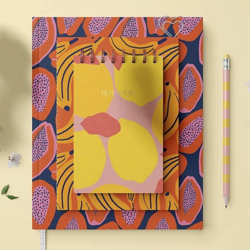 Stationery set mockup featuring a spiral notebook and two flat books with colorful papaya-themed covers on a beige surface.