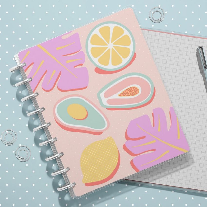Spiral planner mockup featuring a vibrant fruit and leaf cover, stacked on a grid notebook with a pen and binder rings.