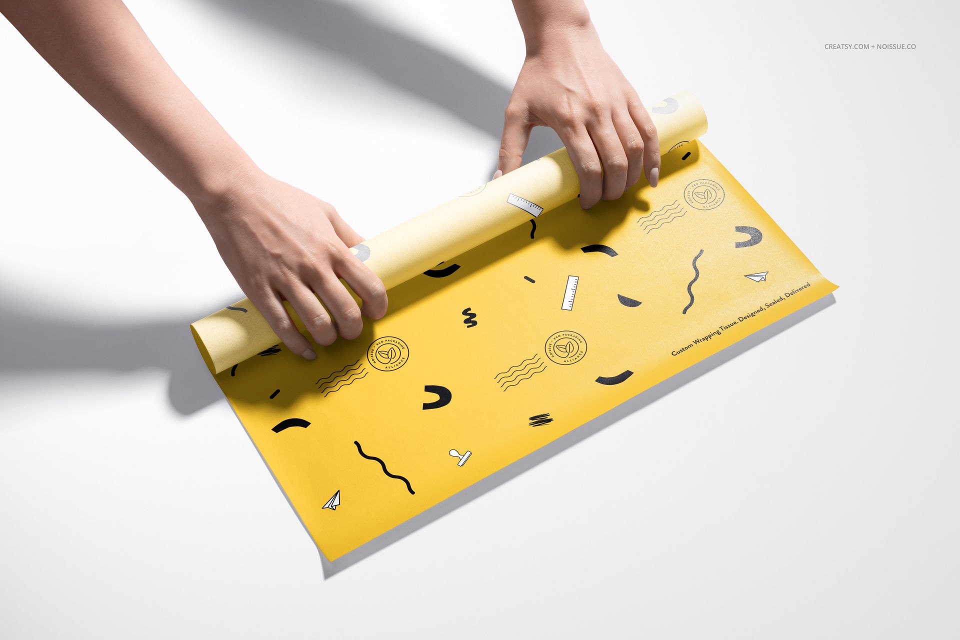 Yellow food safe paper mockup featuring abstract black motifs, being rolled by hands on a clean white background.