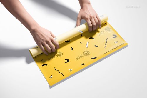Yellow food safe paper mockup featuring abstract black motifs, being rolled by hands on a clean white background.