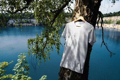 PSD mockup featuring a blank T-shirt suspended on a tree by a lake, surrounded by natural outdoor scenery and foliage.