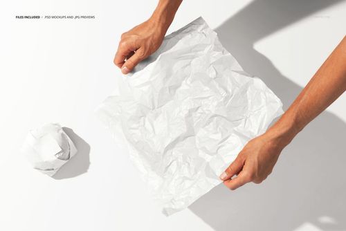 Burger wrapping paper PSD mockup showing hands handling a textured white sheet with a scrunched paper ball beside it.