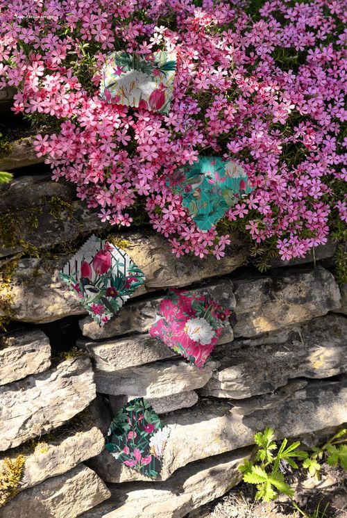 PSD mockup showing assorted fabric swatches with colorful prints placed on a stone wall, accented by pink blossoms.