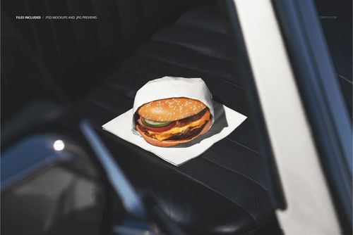 Close-up of a burger in white packaging sitting on a napkin atop a dark leather car seat, PSD mockup scene.