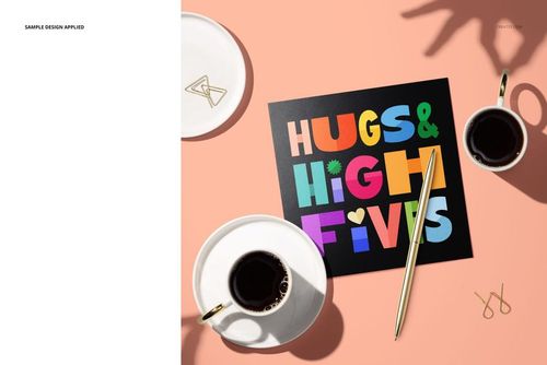 PSD mockup of a square folded greeting card featuring bold multicolored lettering, placed near coffee cups and a pen.