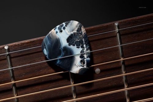Detailed mockup showing a uniquely patterned guitar pick lying across metal strings on the neck of an acoustic guitar.