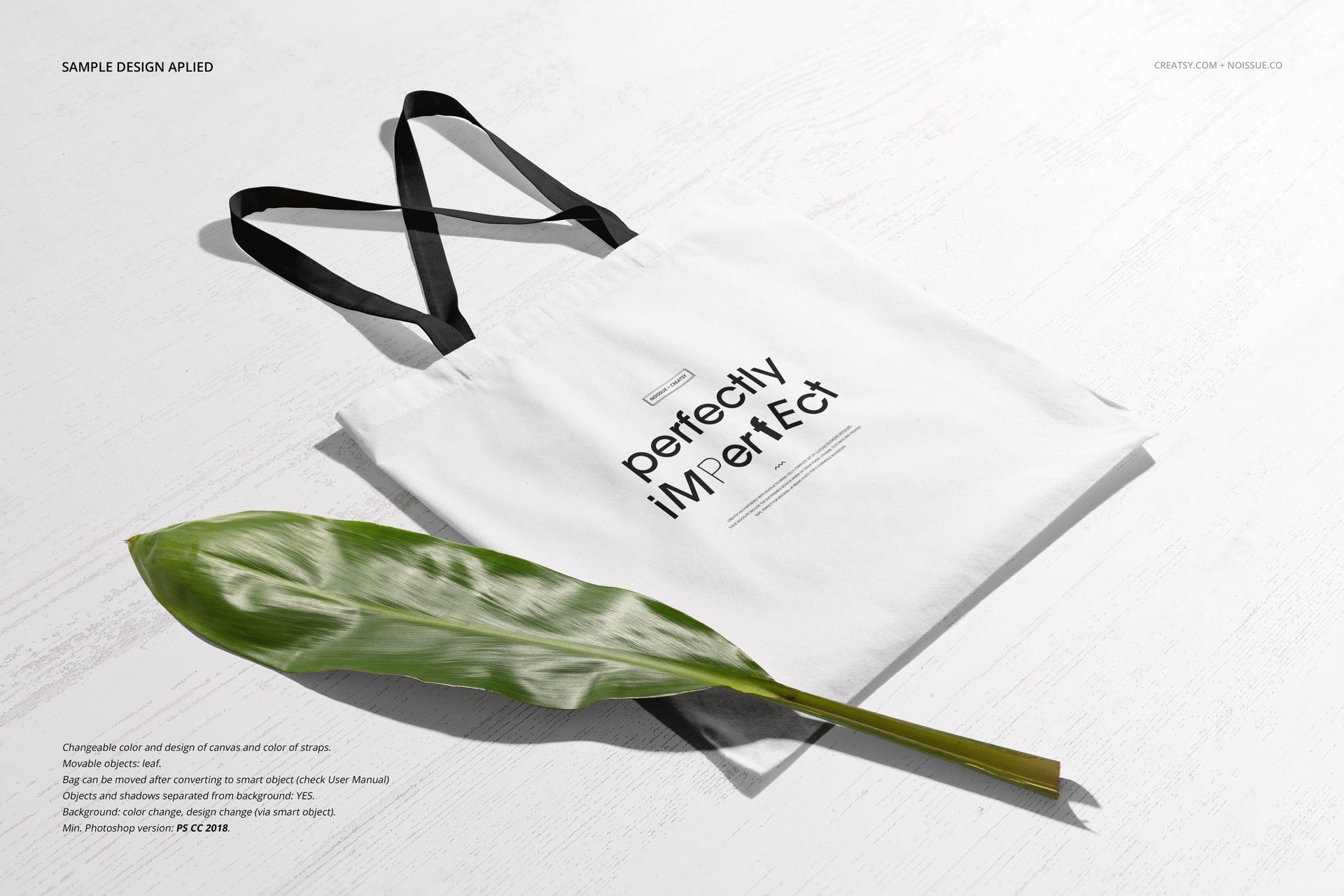 Front view of a PSD mockup showing a white tote bag with black straps and a green leaf as a prop on a white floor.