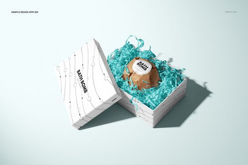 Bath bomb mockup featuring a square white box with abstract lines, open to reveal a brown bath bomb on blue filler.