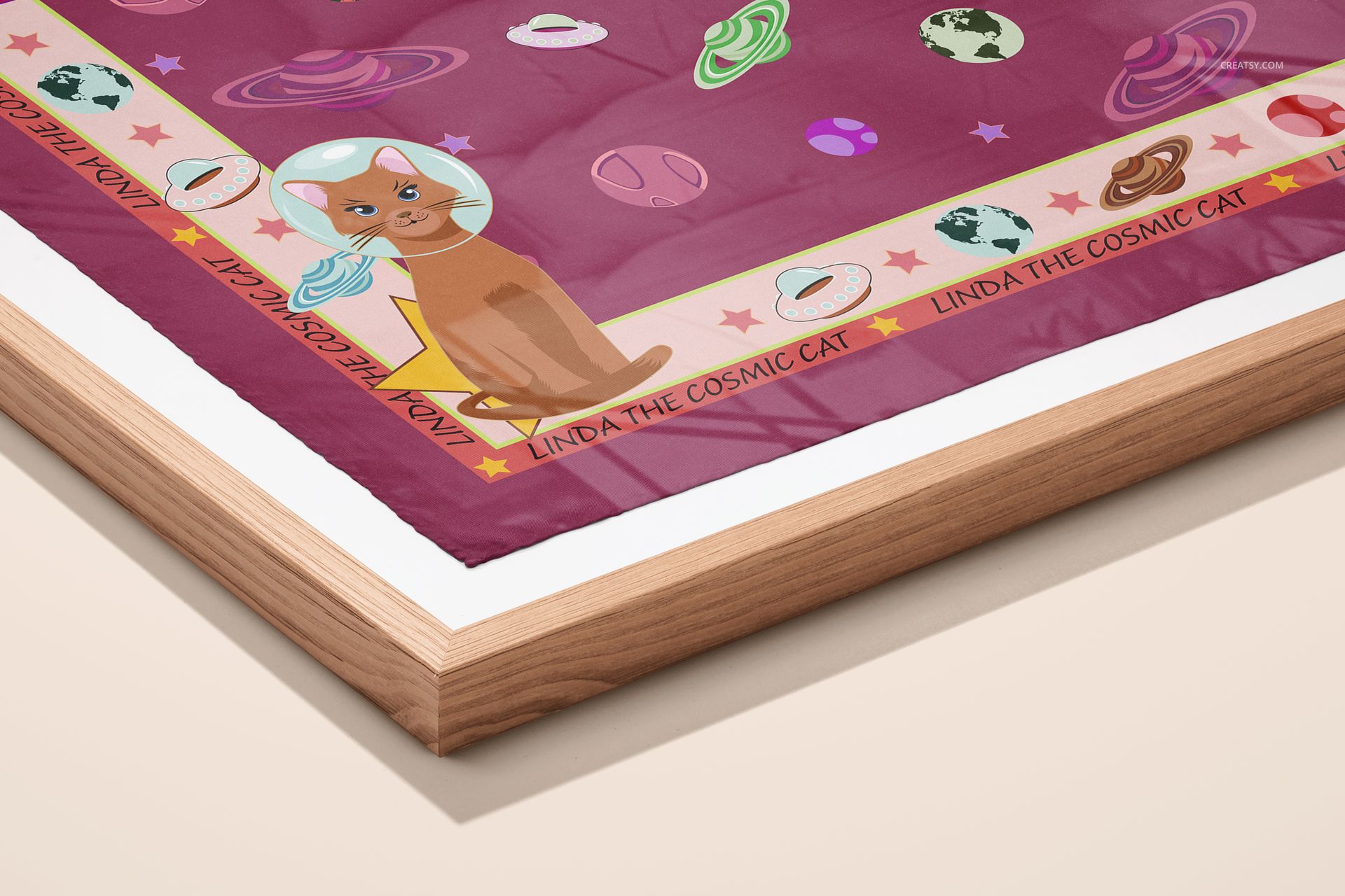 Framed silk scarf mockup featuring space-themed graphics and a cat in an astronaut helmet, shown from an angled perspective.